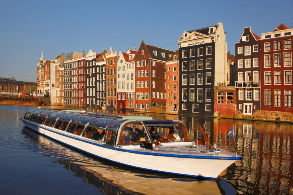 Close-up of a motor boat cruising the canal and passing by the colorful houses in Amsterdam, Netherlands