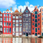 Colorful Amsterdam canal houses line the waterfront, showcasing a vibrant skyline against a clear blue sky