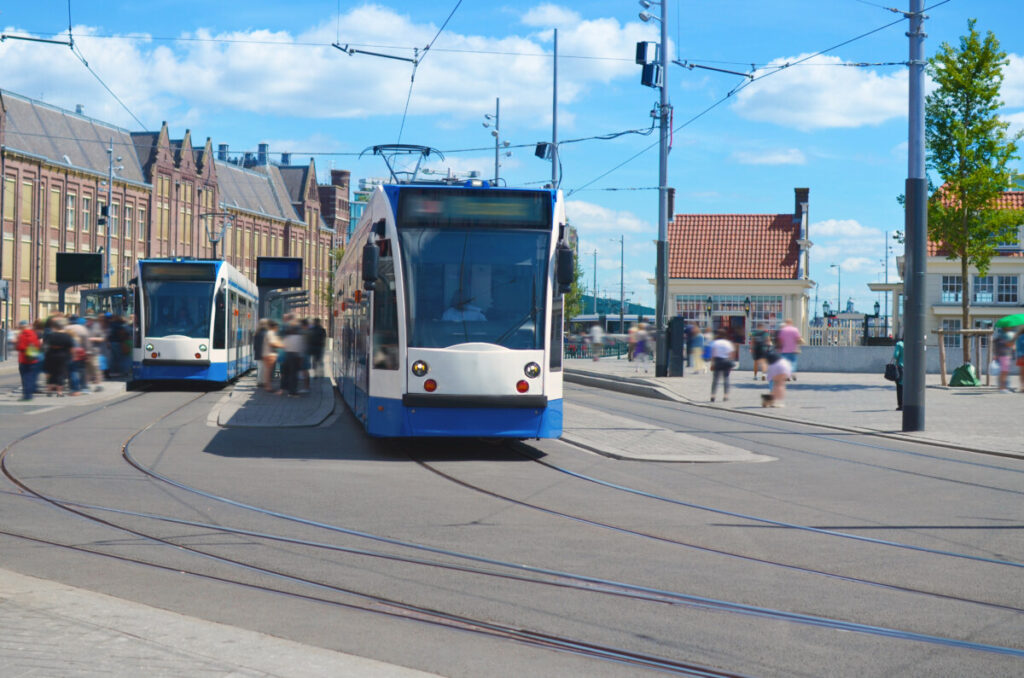 Modern trams and people at tram stop on sunny day in Amsterdam