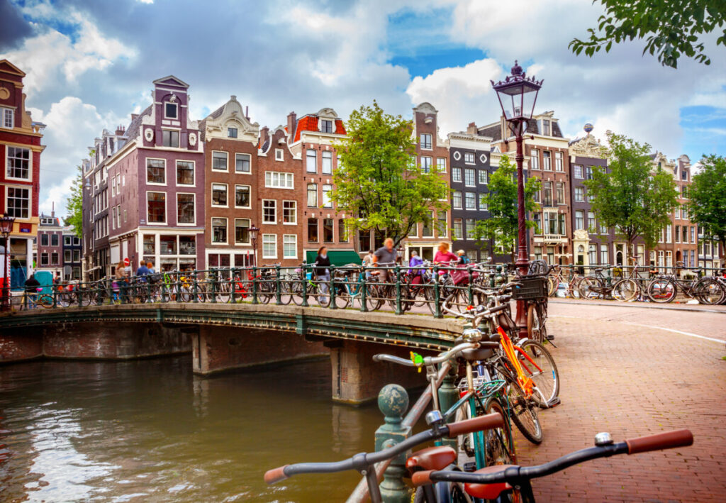 Row of parked bicycles along the canal, with tourists and locals nearby, in Amsterdam, Netherlands