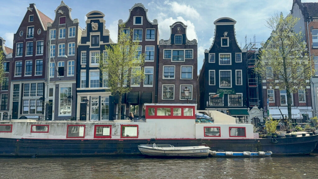 Amsterdam canal houses with boat, featuring tilted facades and diverse gable styles.