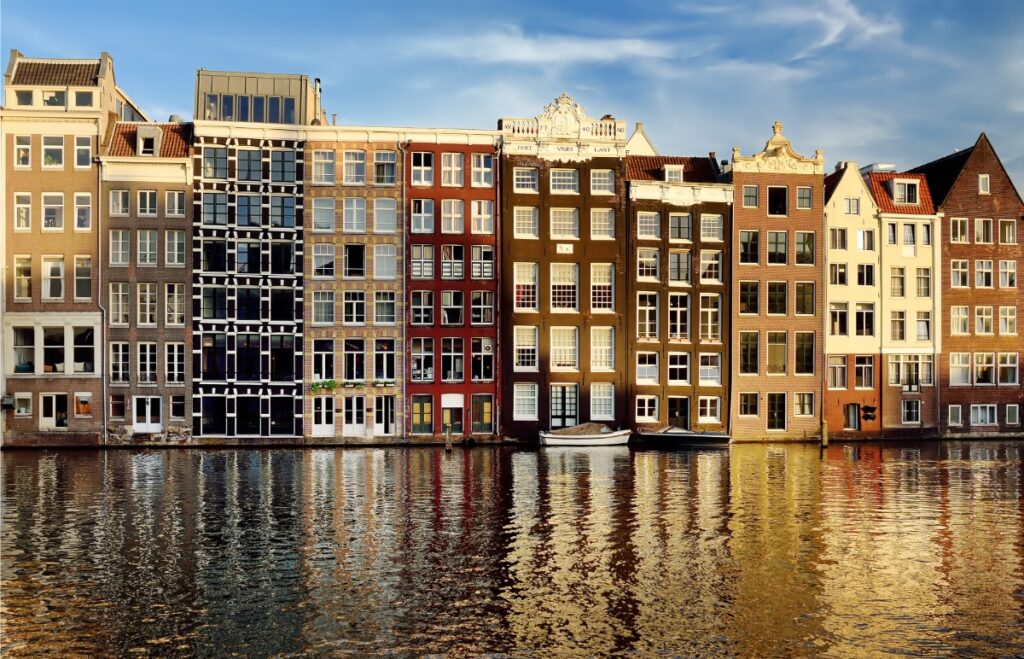 Sunset view of the famous dancing houses along the Damrak canal in Amsterdam, reflecting vibrant colors on the water