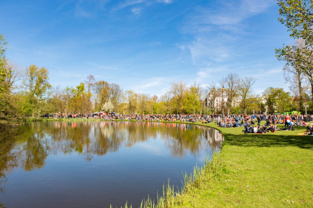 Tourists and locals gather for picnics and relaxation in Vondelpark, enjoying the festive atmosphere of King's Day celebration