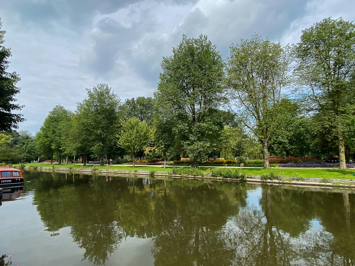 Serene canal view with lush greenery and tour boat in Westerpark, Amsterdam