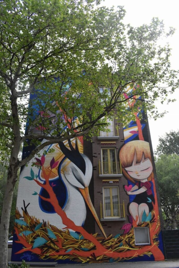Street art by Julieta XLF titled "Wherever You Come From, Here You Are Welcome" displayed on a wall in Amsterdam